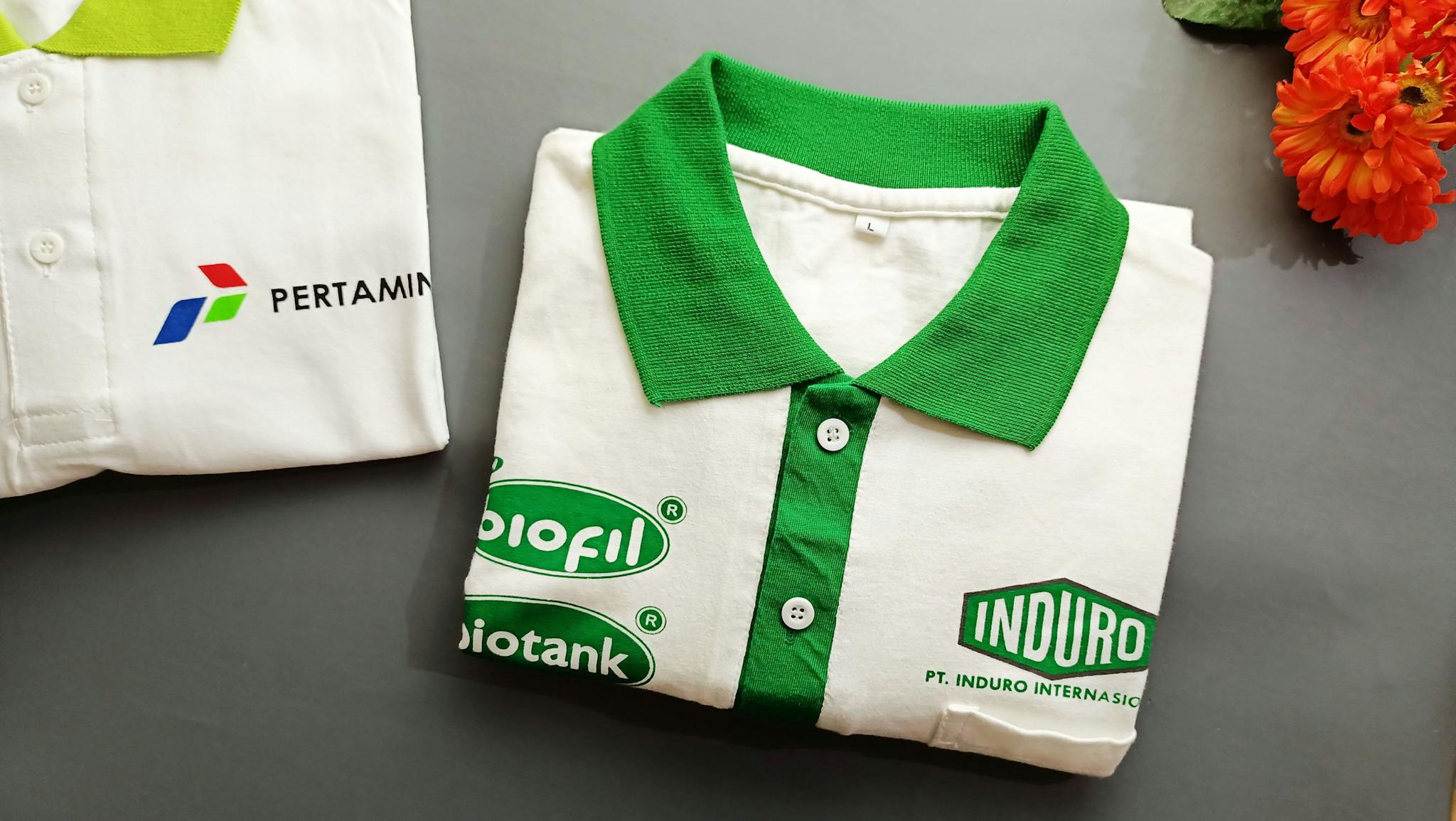 Folded green and white polo shirts with branding logos on a grey background.